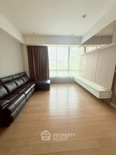 Spacious modern living room with sleek black leather sofa and large windows.