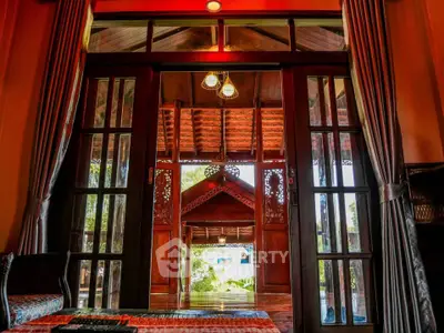 Charming traditional wooden interior with intricate carvings and large glass doors opening to a serene view.