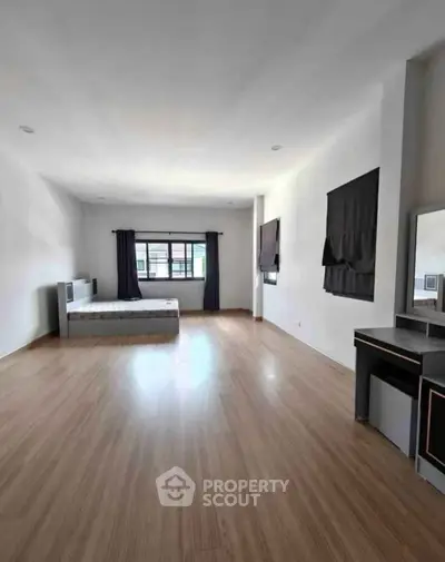 Spacious bedroom with wooden flooring and large window for natural light.