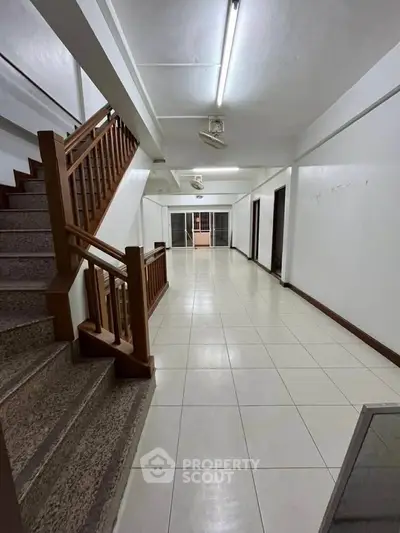 Spacious interior hallway with tiled flooring and wooden staircase, ideal for versatile use.