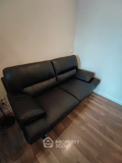 Modern black leather sofa in a cozy living room with wooden flooring.