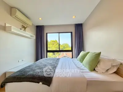 Cozy bedroom with large window and modern decor, offering a serene view of greenery.