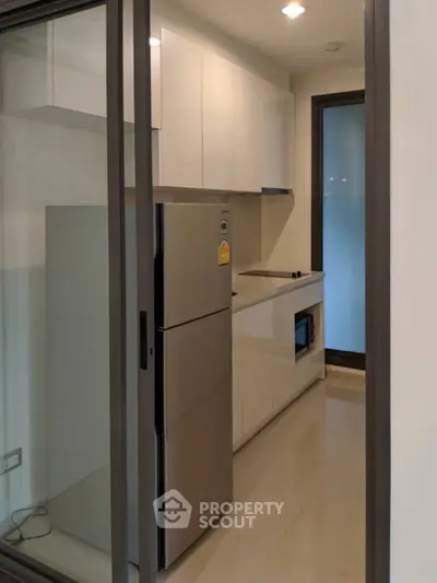 Modern kitchen with sleek cabinetry and stainless steel fridge in compact layout.