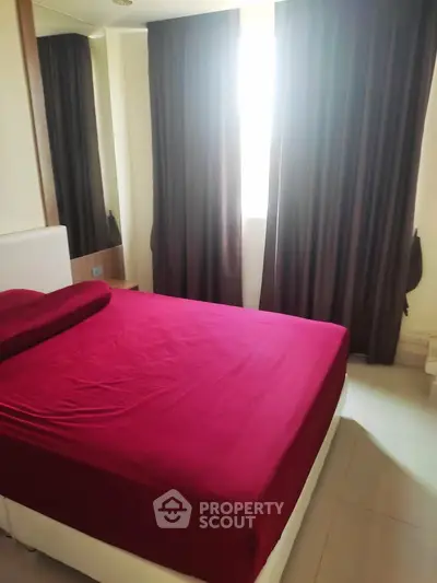 Cozy bedroom with red bedding and dark curtains, perfect for relaxation.