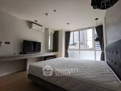 Modern bedroom with large window and city view, featuring a comfortable bed and sleek TV setup.