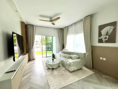 Modern living room with large TV and stylish decor, featuring a cozy sofa and natural light from a balcony view.