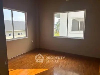 Spacious empty room with wooden flooring and large windows offering natural light.