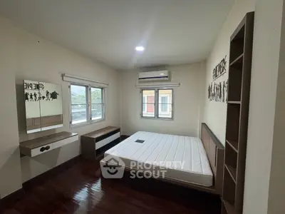 Spacious bedroom with hardwood floors and modern furniture, featuring large windows for natural light.