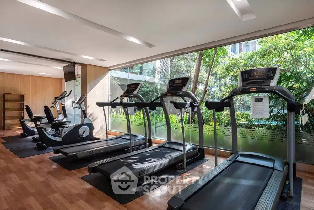 Modern gym with treadmills and exercise bikes in a bright, glass-walled space.