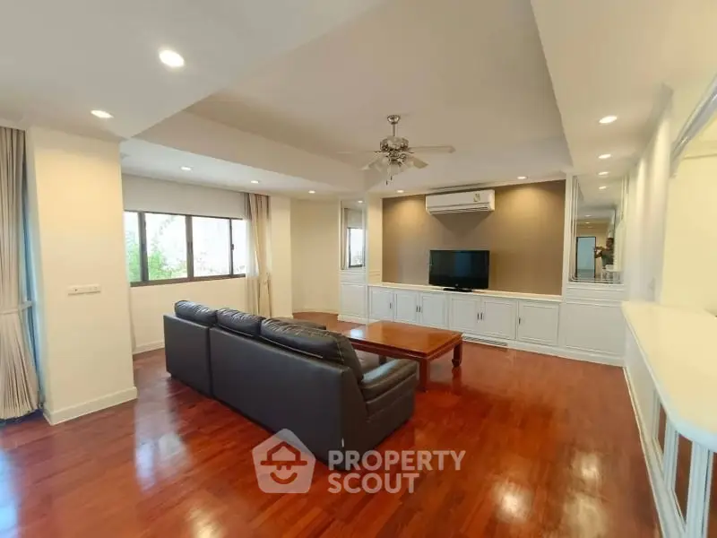 Spacious living room with hardwood floors, large windows, and modern furnishings in a stylish apartment.