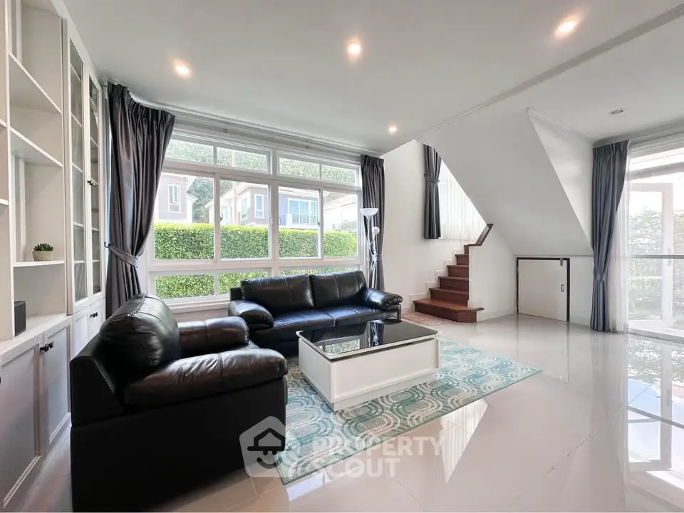Spacious modern living room with large windows and elegant black leather sofas
