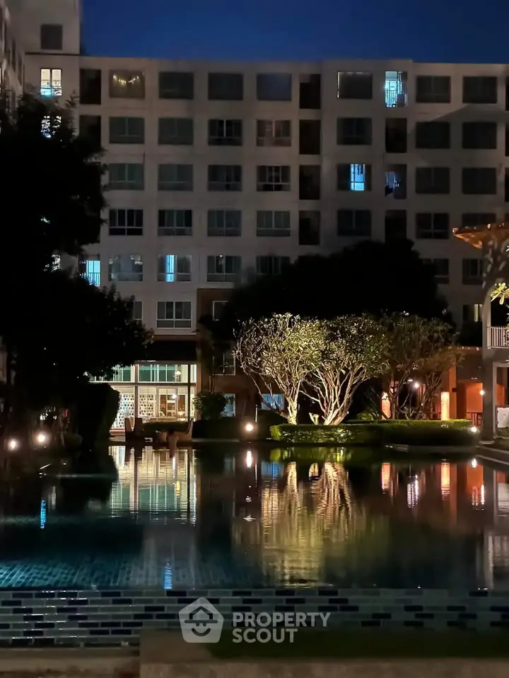 Stunning night view of a modern apartment building with illuminated pool and lush greenery.
