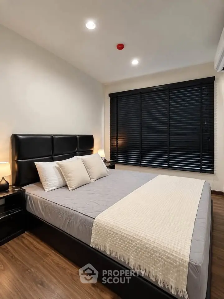 Modern bedroom with sleek black blinds and cozy bedding in a stylish apartment.