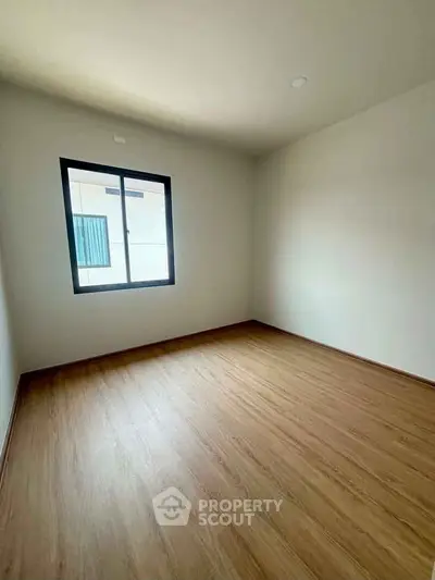 Spacious empty bedroom with wooden flooring and large window, perfect for customization.