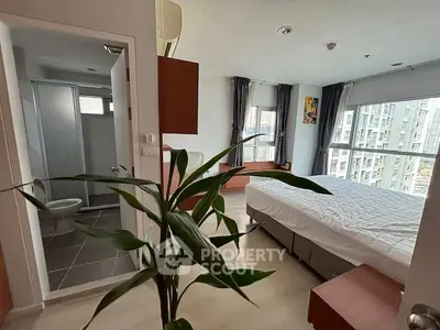 Modern bedroom with large window and city view, adjacent to a compact bathroom.