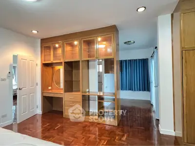 Spacious bedroom with elegant wooden built-in wardrobe and vanity, featuring polished wood flooring and natural light.