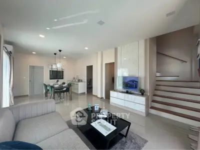 Spacious modern living room with elegant decor and open dining area, featuring a sleek staircase and natural lighting.