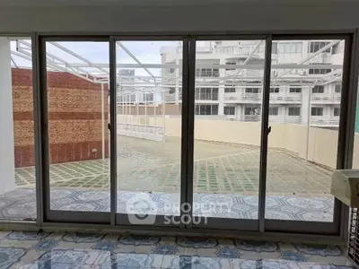Spacious balcony with sliding glass doors offering a view of modern architecture and tiled flooring.