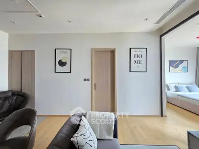 Modern living room with stylish decor and view into a cozy bedroom, featuring elegant furniture and wall art.