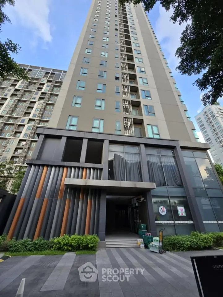 Modern high-rise building with sleek design and lush greenery at entrance