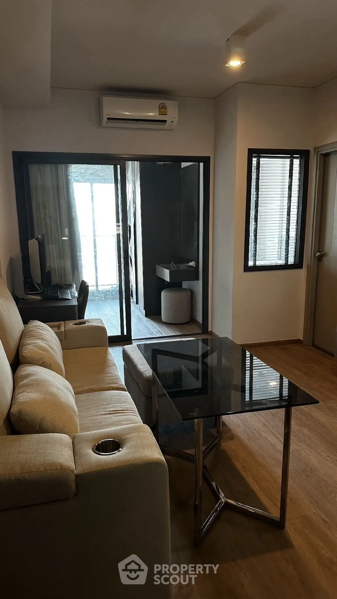Modern living room with glass coffee table and beige sofa, featuring a study area and air conditioning.