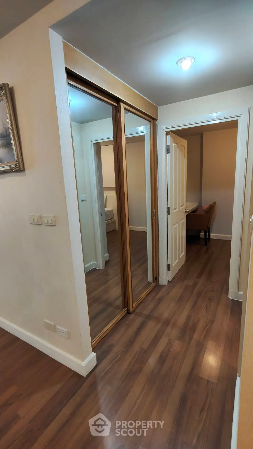 Spacious hallway with wooden flooring and mirrored closet doors in modern apartment.