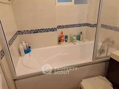Modern bathroom with bathtub and tiled walls, featuring essential toiletries for a comfortable living experience.