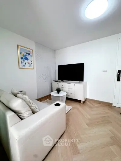 Modern living room with stylish decor and large TV, featuring elegant wooden flooring and cozy seating.