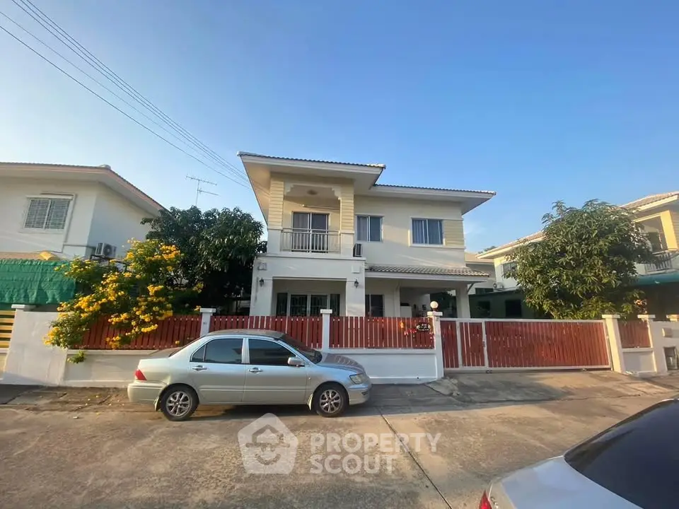 Charming two-story house with red fence and driveway in a sunny neighborhood.