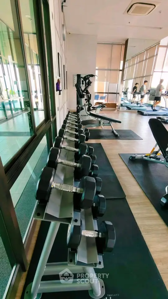 Modern gym with state-of-the-art equipment and floor-to-ceiling windows in luxury apartment building.
