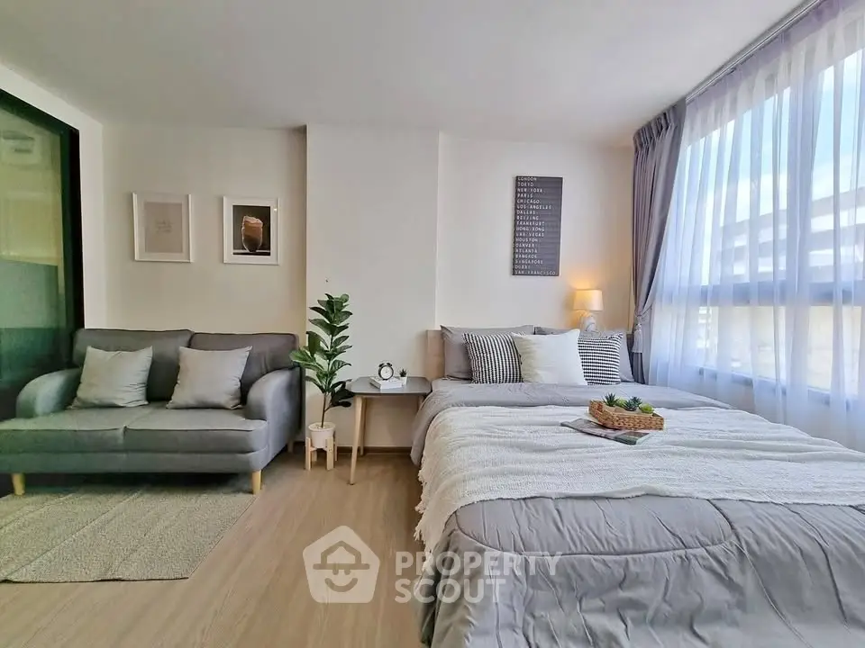 Modern studio apartment with cozy bed and stylish sofa, featuring large windows for natural light.
