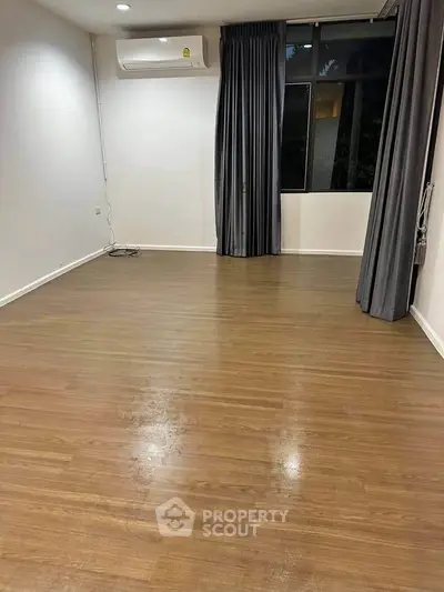 Spacious empty room with wooden flooring and large window, ideal for customization.