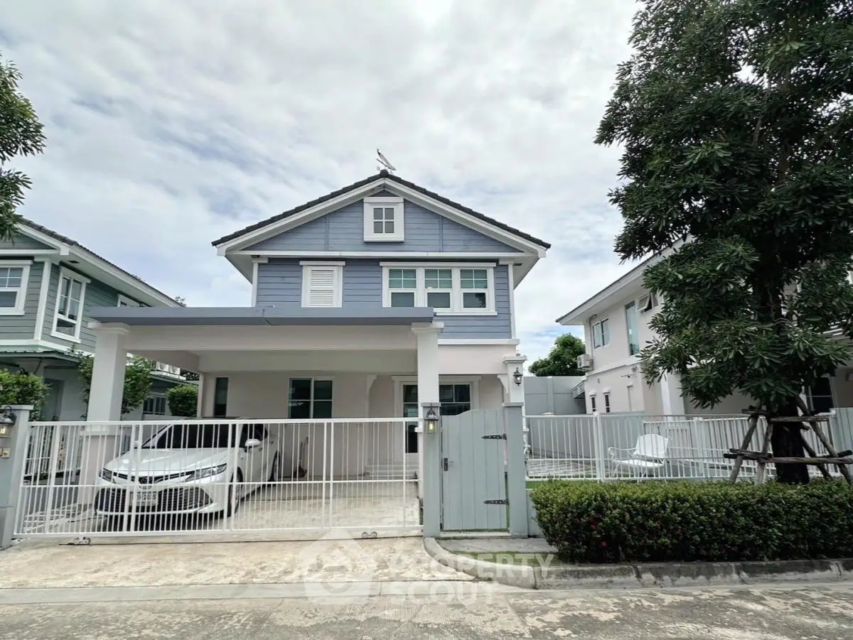 Charming two-story blue house with carport and lush greenery in a serene neighborhood.