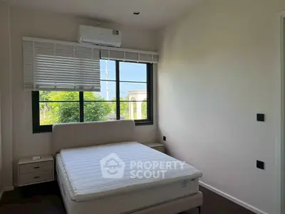 Bright bedroom with large window and modern air conditioning unit, offering a serene view of greenery.