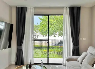 Modern living room with large window and garden view, featuring elegant curtains and cozy seating.