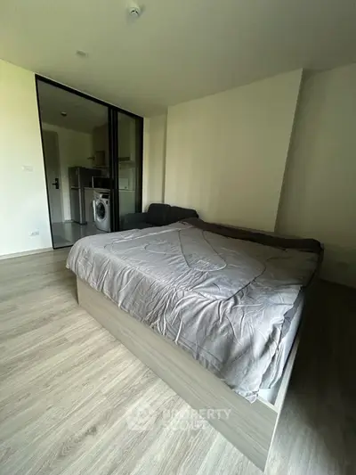 Modern studio apartment with bed, sofa, and compact kitchen featuring a washing machine.