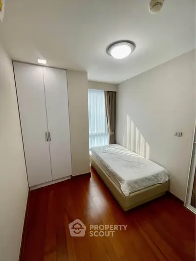 Cozy bedroom with wooden flooring and natural light, featuring a single bed and built-in wardrobe.