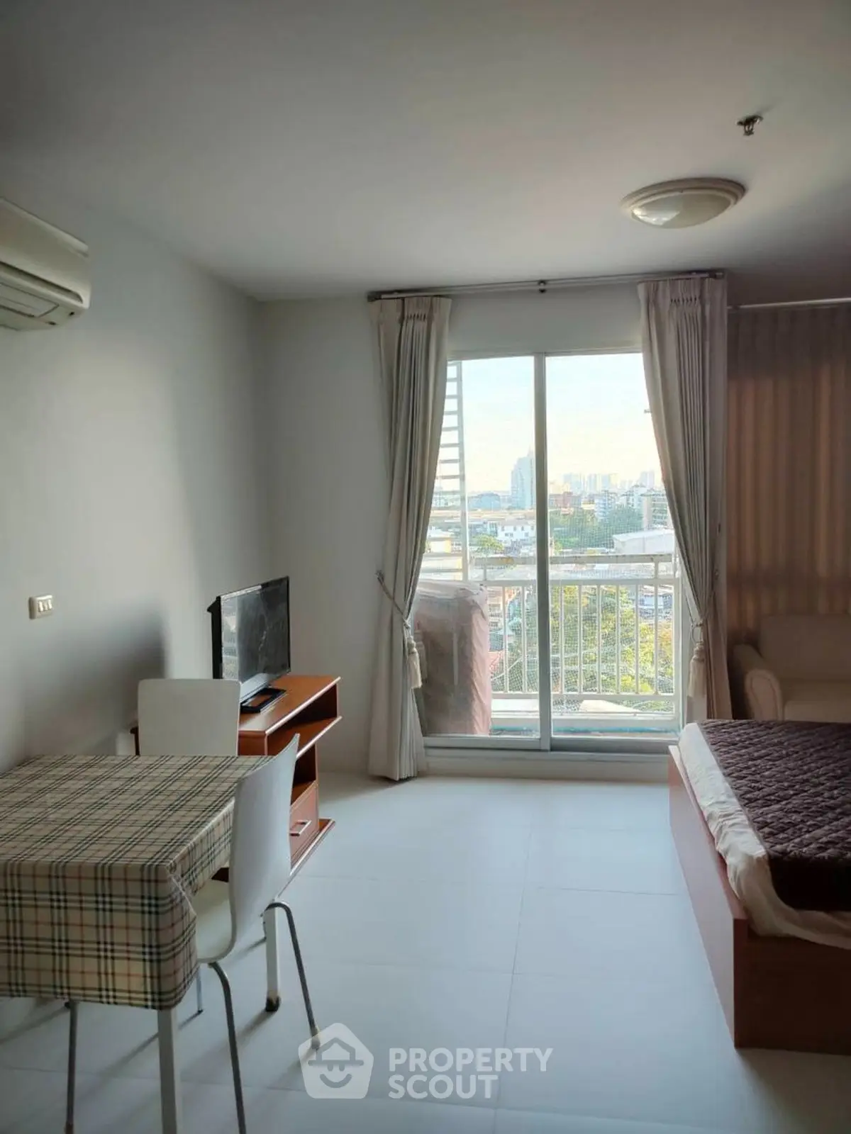 Cozy studio apartment with balcony and city view, featuring a compact living area and modern furnishings.