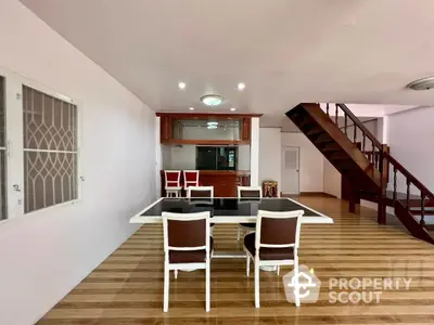 Spacious living room with polished wooden floors, elegant dining set, and a cozy kitchen with a pass-through window, complemented by a stylish staircase.