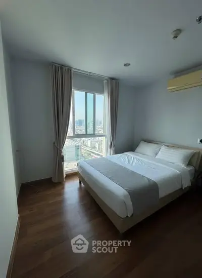 Bright bedroom with city view, featuring a cozy bed and wooden flooring, perfect for urban living.