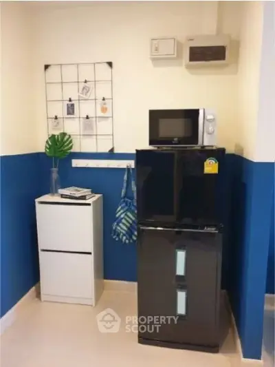 Modern kitchen corner with sleek black fridge and microwave, vibrant blue walls, and stylish storage solutions.