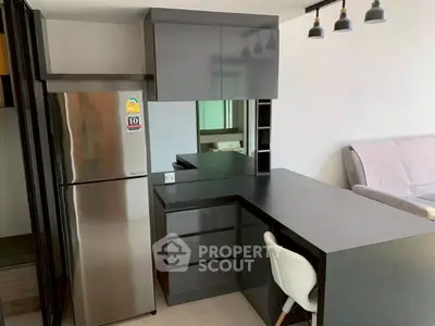 Modern kitchen with sleek black cabinetry and stainless steel fridge in open layout apartment.