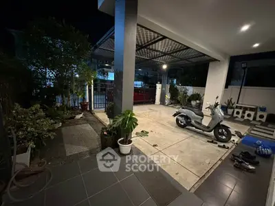 Spacious modern home entrance with covered parking and lush greenery at night.