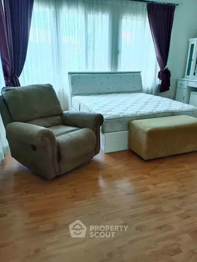 Spacious bedroom with large window, cozy armchair, and elegant curtains.