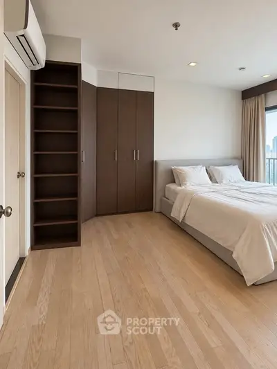 Spacious modern bedroom with wooden flooring and built-in wardrobe, offering a serene city view.