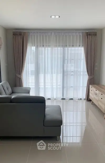 Modern living room with sleek sofa and large window draped with elegant curtains.