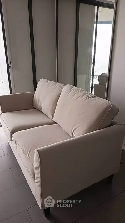Elegant beige sofa in modern living room with large windows and sleek flooring.