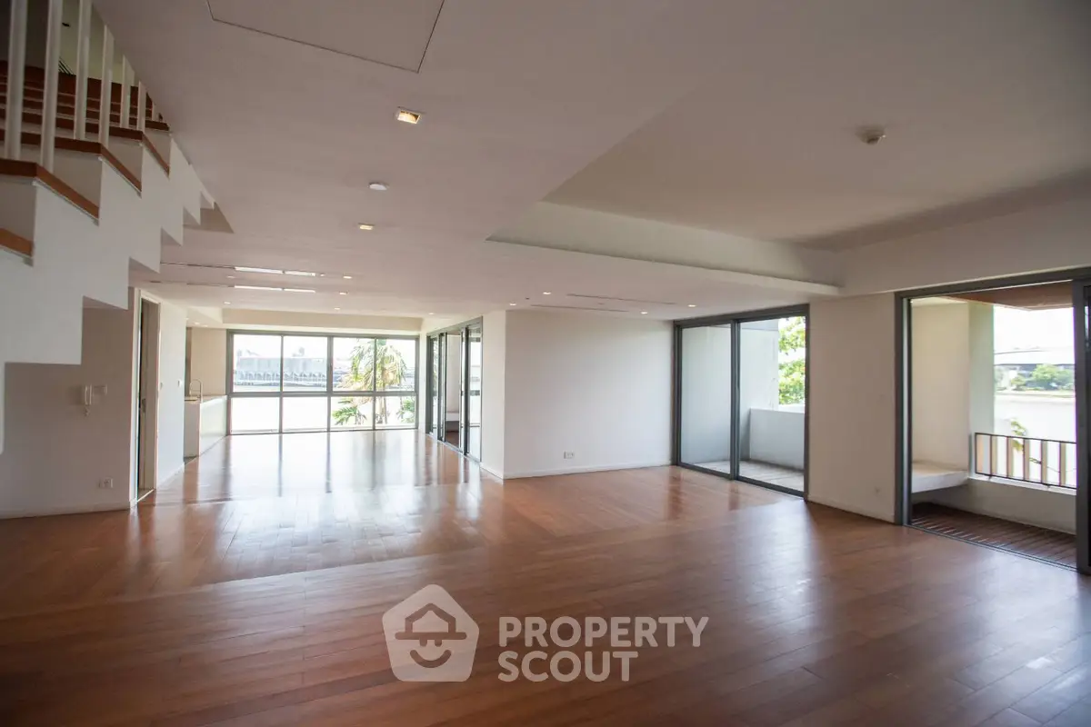 Spacious open-plan living room with wooden floors and large windows offering natural light.