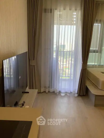Modern living room with large window and TV, featuring elegant curtains and light wood flooring.