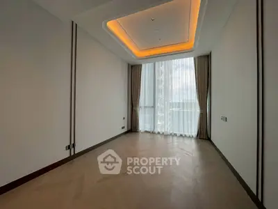 Spacious empty room with elegant ceiling lights and large window offering natural light.